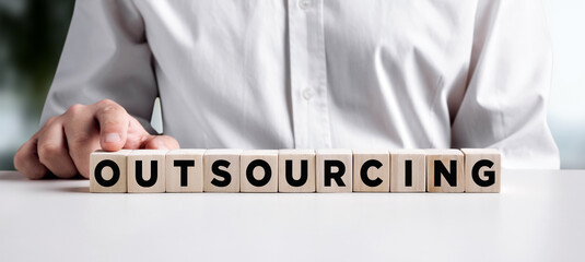 Businessman pressing his finger on the wooden cubes with the word outsourcing.