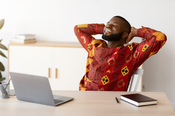 Cheerful African Guy In Traditional Shirt Leaning Back In Chair At Workplace
