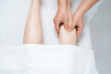 Close-up top view of male masseur with strong hands massaging lower part of leg to young woman lying on massage table on white background. Concept of massage spa treatments