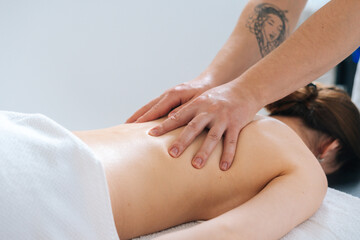 Close-up view of male masseur massaging back and shoulder blades of female lying on massage table at spa salon. Beautiful young woman with perfect skin getting relaxing massage.