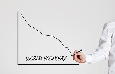 Businessman draws a declining line graph with the word world economy. World economic crisis