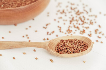 Buckwheat kernels in wooden bowl and spoon on white background. Top view. Copy, empty space for text