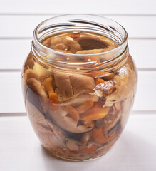 A jar of homemade pickled wild mushrooms on a white wooden table. Traditional Russian snack.