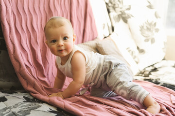Portrait of a child, a six-month-old baby crawling on the couch and smiling. Childhood and Parenthood concept