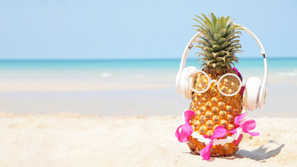 Summer party. Pineapple wearing sunglasses and listen to music on beach and blue sky background. Tropical fashion. Summer Fashion on holiday concept.