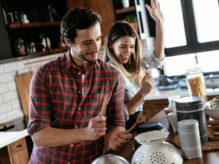 Young couple playing with kitchen utensils. Boyfriend and girlfriend having fun while preparing food.