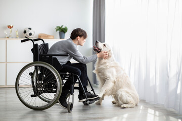 Positive handicapped adolescent playing with his dog, petting golden retriever at home