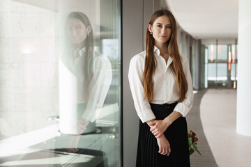 Fototapeta na wymiar Successful young attractive businesswoman building own carrier at design company, standing near window in office corridor, smiling and looking camera, speaker awaiting start of presentation