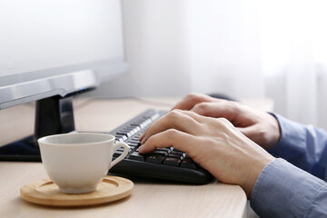 Man sitting at PC keyboard with coffee cup. Break during work in office