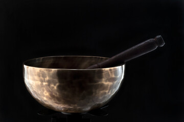 A bronze Tibetan singing bowl with a stick on a black background.