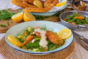 Fish dinner with breaded fish, vegetables, potatoes and dill sauce