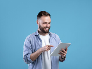 Joyful bearded man using tablet computer for online work or studies on blue studio background