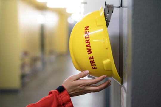 Action of fire fighter is taking a "Fire Warden" safety yellow hardhat helmet that hang on the wall, Response for emergency situation. Close-up and selective focus at the human's hand.