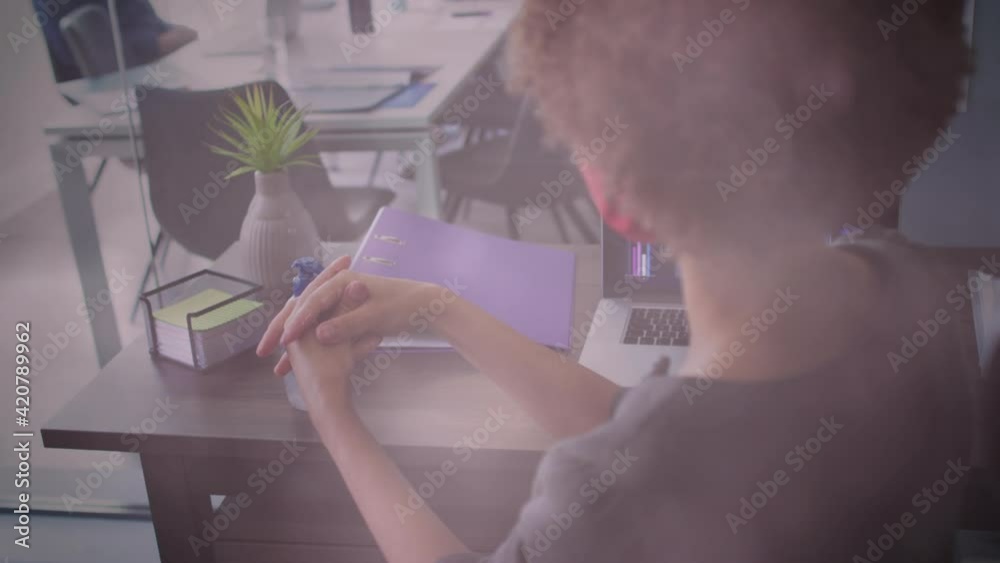 Poster Animation of glowing lights over woman sanitizing her hands in office wearing face mask