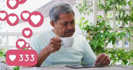 Animation of heart love icons over senior man using tablet, drinking coffee at home - Powered by Adobe