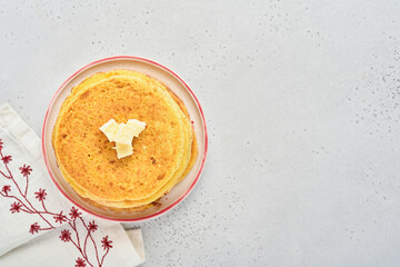 Crepes or thin pancakes stack with butter and raspberry jam on beautiful ceramic plate on an old gray concrete background. Top view, copy space. Homemade thin crepes for breakfast or dessert.