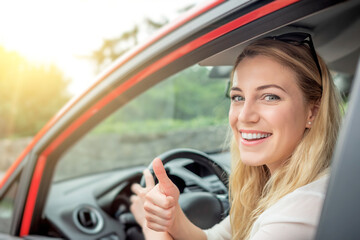 Happy beautiful woman is driving a red car.