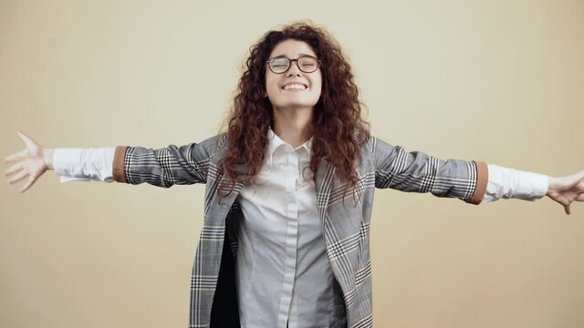 Hey come here to get you dressed. The happy, in love young woman offers hugs to everyone. Cretaceous in gray jacket and white shirt, with glasses posing isolated on a beige background in the studio