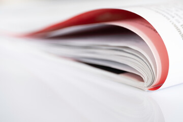 Folded magazine with red page reflected on a white surface with shallow depth of field
