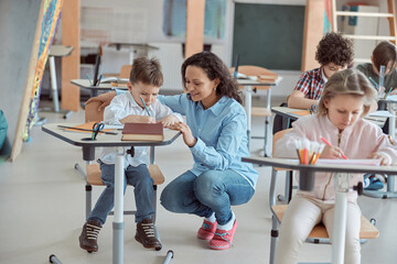 Happy kind teacher is helping kids in elementary school lessons