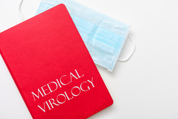 Fototapeta na wymiar Medical mask and Medical Virology textbook, cropped image, top view, copy space