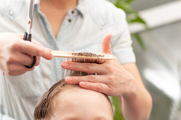 caring female hands of a mother with a comb and scissors make a fashionable haircut for her son at home during the second lockdown. selective focus