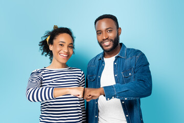 joyful african american couple doing fist bump while looking at camera on blue