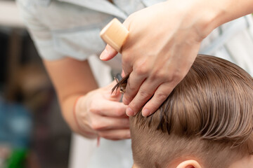 caring female hands of a mother with a comb and scissors make a fashionable haircut for her son at home during the second lockdown. selective focus