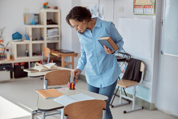 Happy afro female teacher with book in a light elementary school classroom