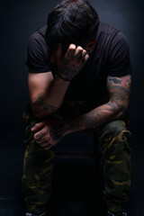 High contrast picture of a bearded male model sitting on a chair and covering his face with his...