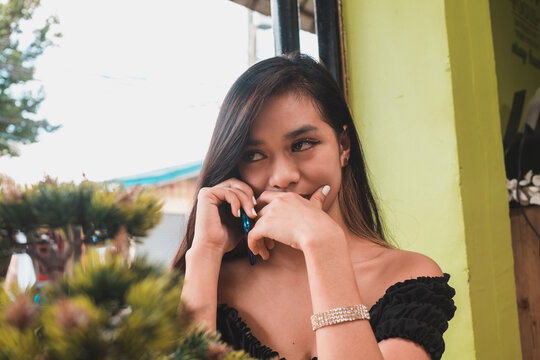 A pretty and slim young lady gossips on the phone and trying to contain her giggling.