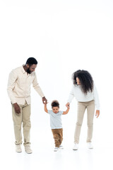 happy african american couple holding hands of toddler son walking on white