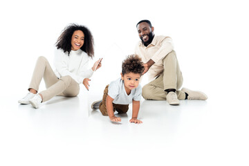 Fototapeta na wymiar happy african american couple holding paper roof above crawling son on white