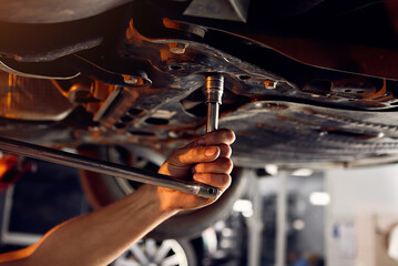 Handsome auto mechanic checking running gear of automobile on service station. Cheerful male worker fixing problem with car. Concept of problem solving