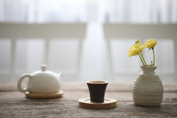 Small tea cup and teapot with flower vase on wooden table