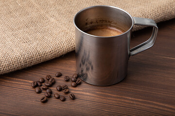 Metallic old-school cup with black coffee made in it placed on a wooden table