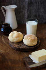 Brioche on a wooden background with a glass of milk, a white jug, butter. Bun. Side view.