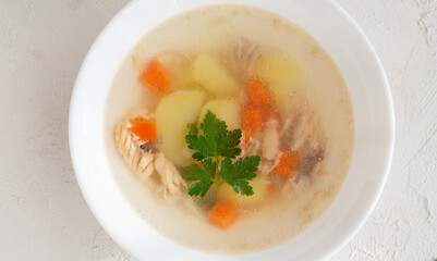 Clear fish soup with pieces of vegetables and percussion in a white bowl on a white plate. Healthy food concept. Close-up. Horizontal orientation.