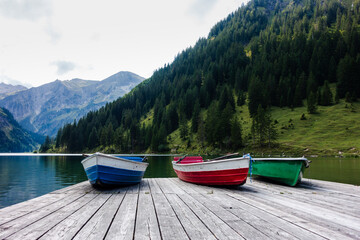 Three rowing boats laying on a wooden landing stage at an idyllic mountain lake in the alps. Low angle view, front view.
