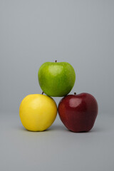 red yellow and green apples stacked in 
triangle on a grey background.