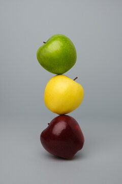Apples of different colors stacked on top of each other in balance on a grey background.