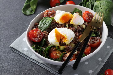 Salad with quinoa, spinach, poached eggs and cherry tomatoes in a plate on gray background. Healthy eating. Close up