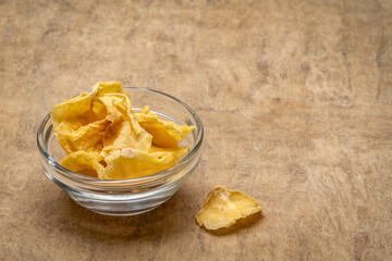 Dried slices of yacon tuber in a small glass bowl against handmade bark paper with a copy space. Yacon contains inulin, a complex sugar, which promotes healthy probiotics. Superfood concept.