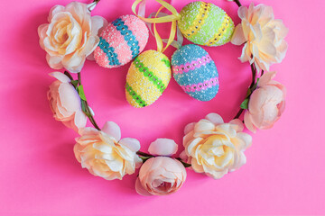 easter decor. Decorated eggs and wreath of flowers on bright pink background. Close-up of multi colored easter eggs and flowers
