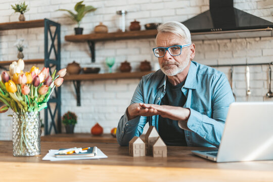 Protecting your home. Senior gray-haired man holds his hands over houses. Safe purchase, security of real estate.