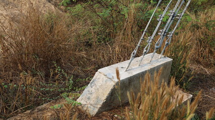 Suspension anchors for electric poles. Concrete base with anchor connected to guy wire for tensioning of high voltage poles on dry grass background with copy area. Selective focus