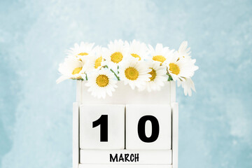 cube calendar for March with daisy flowers over blue with copy space