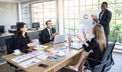 Collaboration is a key to best results. Group of young modern people in smart clothing wear planning business strategy while young man pointing at infographic displayed on the glass wall in the office