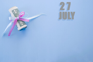 calendar date on blue background with rolled up dollar bills pinned by blue and pink ribbon with copy space. July 27 is the twenty-seventh day of the month