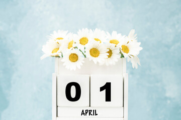 cube calendar for April with daisy flowers over blue with copy space